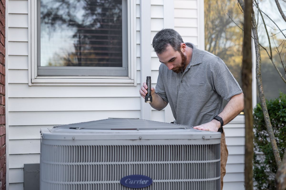 HVAC technician inspecting an outdoor unit at a home