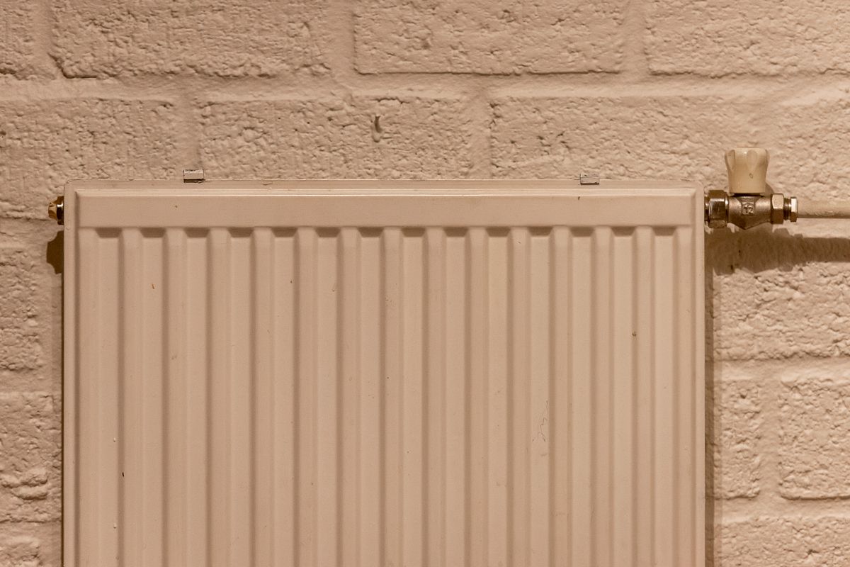 White heating radiator mounted on a brick wall