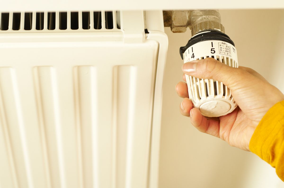 Hand adjusting a thermostat valve on a home radiator